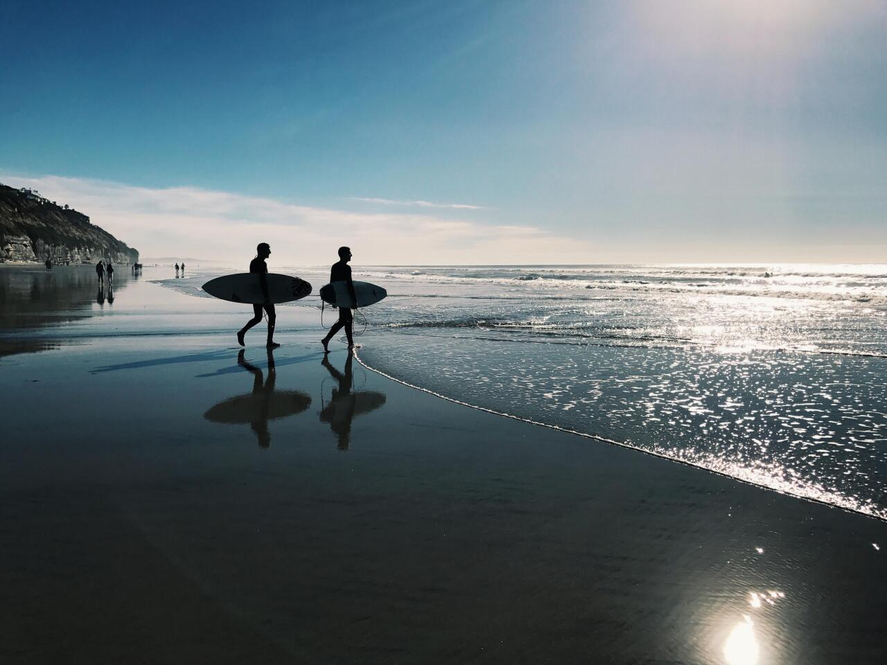 #10. San Diego People walking with surfboards on beach.